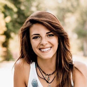 Young woman in white tank top smiling outdoors