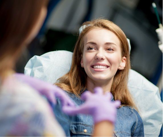 Young woman in dental chair smiling at her dentist