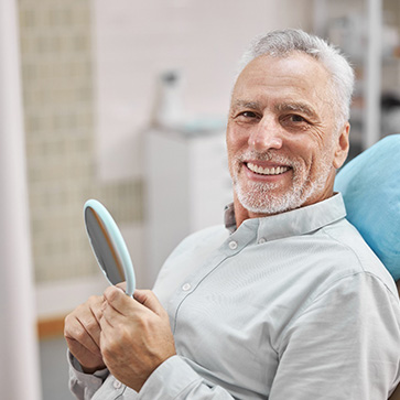 man smiling while holding dental mirror 