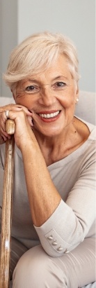 Smiling senior woman holding cane while sitting