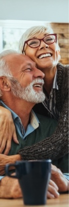 Older man and woman hugging while sitting at table with coffee mug