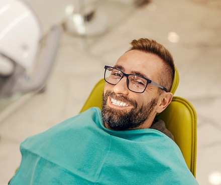 Man with glasses smiling while sitting in treatment chair