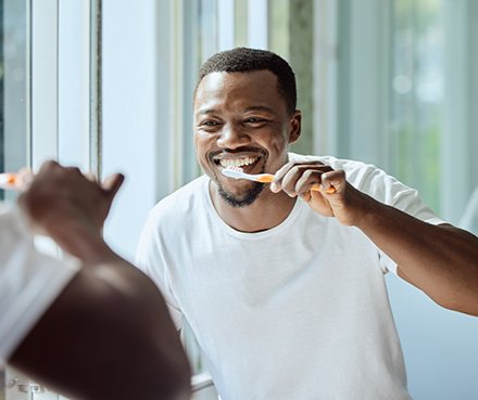 Man smiling while brushing his teeth