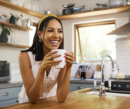 Woman smiling while drinking coffee in kitchen