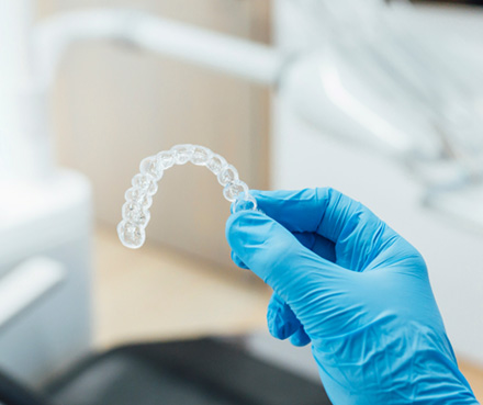 Dentist with blue glove holding clear aligner