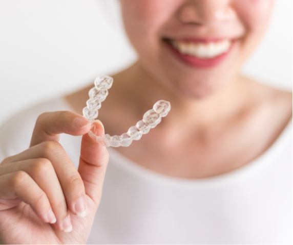 Smiling woman holding an Invisalign clear aligner