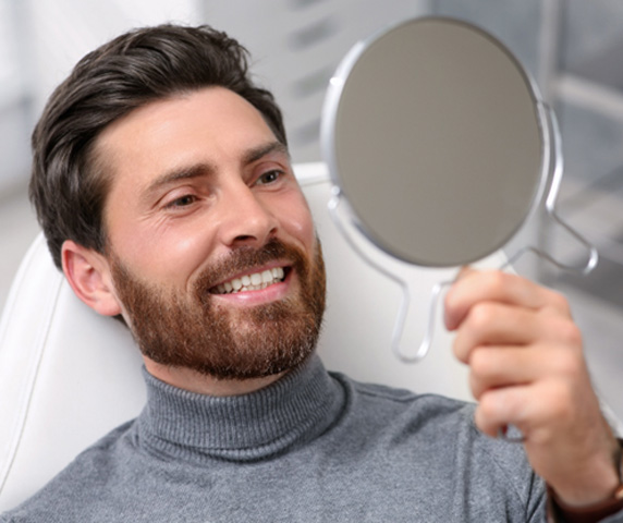 Patient looking at their smile in the mirror and appearing pleased 