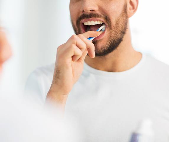 Man in white shirt smiling while brushing his teeth