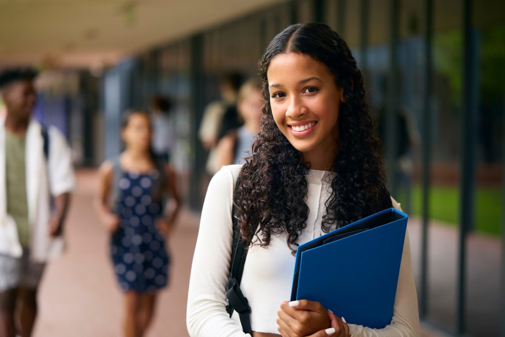 Teen girl smiling while holding folder on campus